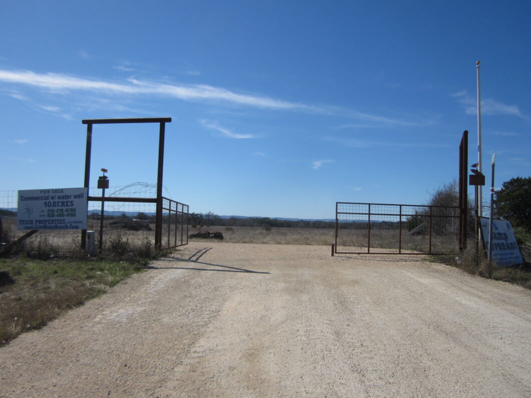 A dirt road with a metal gate and fence.